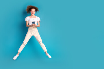 Full size photo of pretty young girl jumping hold device wear trendy white outfit isolated on blue color background