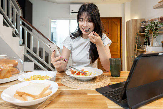 Young Asian woman having breakfast and having online meeting on tablet