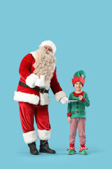 Santa Claus and cute little elf with milk and cookies on blue background