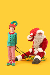 Santa Claus and cute little elf sledding on yellow background