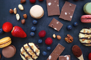 Macarons, chocolate, cookies, berries and various nuts on dark blue background. Top view.