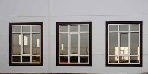 Three windows on a building with a brown frame