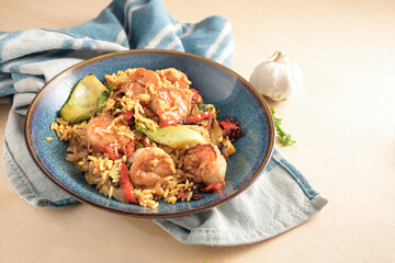 Shrimps or prawns with rice and vegetables on a blue plate and a kitchen towel on a light wooden background, healthy cooking at home, selected focus