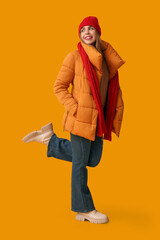 Beautiful young happy woman in warm winter clothes on yellow background
