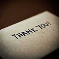 A printed "THANK YOU!" on a textured brown card with soft lighting, offering a warm and formal expression of gratitude