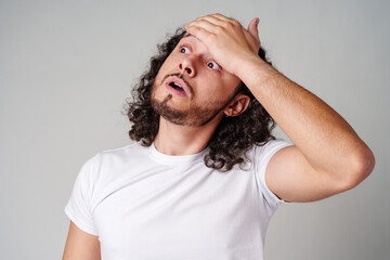 A man with curly hair expresses surprise while looking upwards in a neutral background