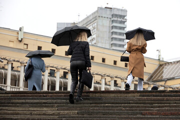 People with umbrellas climb the steps on a street. Rainy weather in autumn city