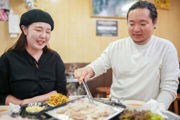 A Korean man and a Japanese woman, both in their 30s and a married couple, are enjoying a meal of Samgyeopsal at a famous restaurant in Jung District, Seoul, Korea, on an autumn night in October.