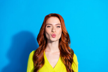 Fototapeta premium Photo of flirty adorable girl with ginger hairstyle dressed yellow knit cardigan send air kiss to you isolated on blue color background