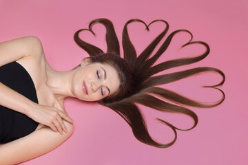 Beautiful young woman with hair in shape of hearts on pink background