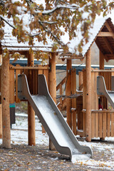 The first snow in the autumn park.A cloudy November day.Yellow foliage on the trees, playground in the snow, autumn landscape.