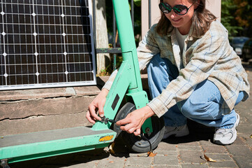 Woman connecting solar panel to electric scooter, highlighting practical application of sustainable...