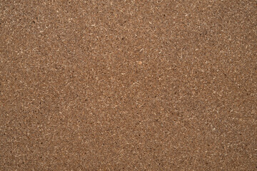 Close-up of a brown cork board surface showing its rough texture and visible fibrous particles, ideal for backgrounds or textures.