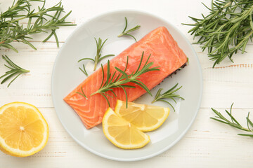 Red fish. Raw salmon fillet with rosemary and lemon on grey plate on white background.