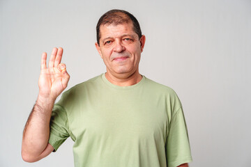 A man with a slight smile making an OK hand gesture against a neutral background