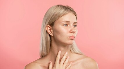 Naklejka premium Young blonde woman posing at camera, massaging face line and temples, isolated on pink studio background. Beauty skin care concept