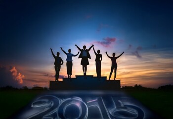 Fototapeta premium Silhouettes of women raise their hands in victory on a platform against a colorful sunset.