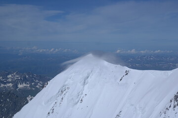 A stunning rock formation covered in snow, set against a clear blue sky with fluffy clouds in the...