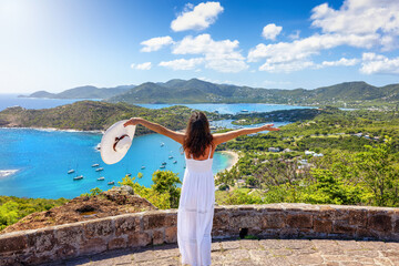 A happy tourist woman in a white dress enjoys the panoramic view over the landscape of Antigua...