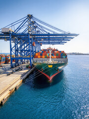 Front view of a large container cargo vessel beeing loaded and unloaded by large cranes in a...