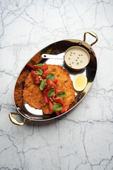 Fried sliced wiener schnitzel on a frying pan with herbs