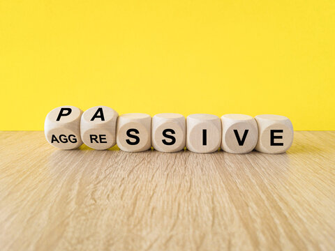 Passive or aggressive symbol. Turned wooden cubes and changes the word passive to aggressive. Beautiful wooden table, yellow background. Business, psychological passive aggressive concept.