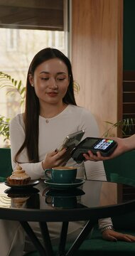 Young Asia female self service use mobile phone pay contactless with credit card reader machine at cafe restaurant. Owner small business, cashless technology and money transfer concept.