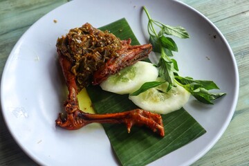 Fried chicken thighs with green chili sauce on top on a white plate close up view.