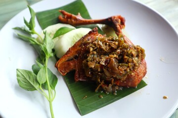 Fried chicken thighs with green chili sauce on top on a white plate close up view.