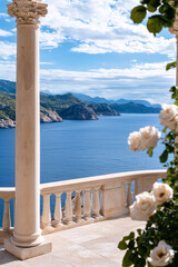 White roses near stone balcony open to stunning sea view under clear sky.