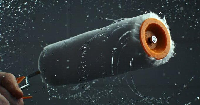 Super slow motion macro of paint roller is being spinned with splashes of color and water isolated on soft background at 1000 fps.