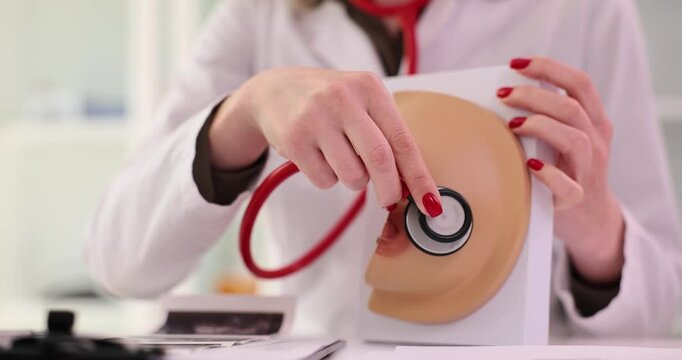 Doctor applies stethoscope to realistic breast model in clinic. Diseases of mammary glands causes prevention and treatment