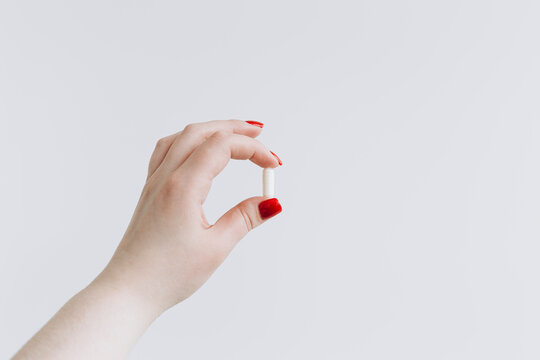 Female hand holding a capsule on a white background
