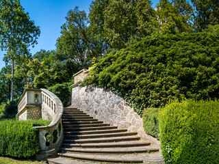 Stone staircase adorned with an ornate railing and lush greenery amidst Römischer Garten in Hamburg Blankenese, a tranquil park setting perfect for travel, tourism or landscaping inspiration content.