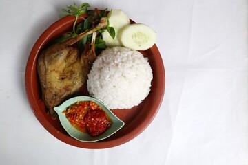 Traditional Indonesian fried chicken with fresh vegetables and chili sauce, served on a wooden plate, isolated on a white background, top view.