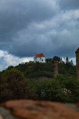 A small white church, on a green mountain, against the background of a rainy sky in the Czech Republic
