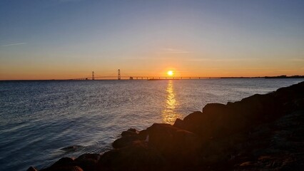 Sunset over the sea with a bridge in the distance.