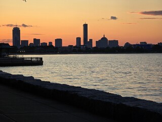 Boston skyline at sunset with silhouetted buildings and calm waterfront.