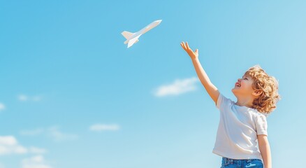 青空に飛ぶ紙飛行機に手を伸ばす笑顔の少年