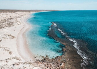 Aerial view of a pristine beach with turquoise waters and white sand dunes.