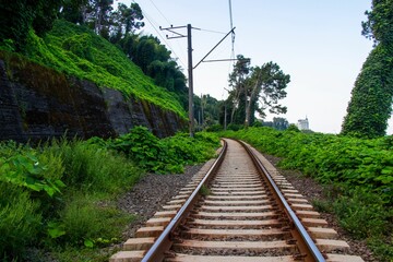 Fototapeta premium Scenic railway track surrounded by lush green vegetation and trees, with a distant building visible