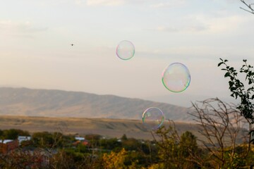 Soap bubbles floating in the air over a scenic landscape with distant mountains and a clear sky.