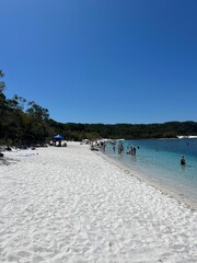 Obraz premium Tropical sandy beach with people swimming in blue calm water on a sunny day