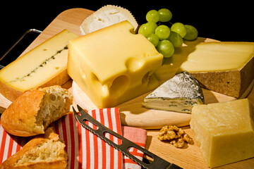 assortment of cheese with bread, grapes, walnuts, cheese knife and striped kitchen towel on wooden...