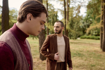 Fototapeta premium Two handsome men dressed elegantly in autumn outfits wander through a tranquil field surrounded by nature.