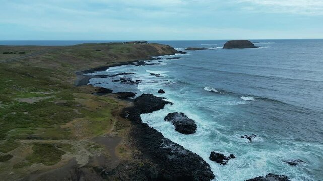 Drone footage showing waves splashing shorelines in Philip Island, Australia with gray cloudy sky