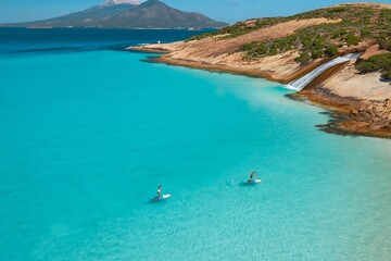 Fototapeta premium Paddleboarding in crystal clear turquoise waters near scenic coastal landscape.