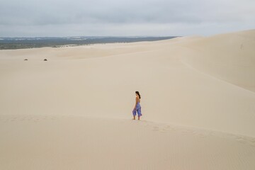 Woman walking on sand dunes under cloudy sky