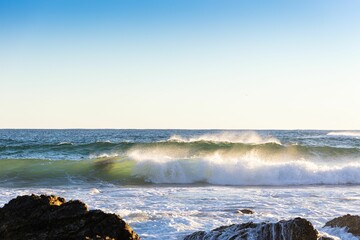 Waves crashing on a rocky coastline under a clear blue sky