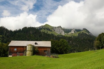 Obraz premium Rustic barn in a green field with mountainous backdrop